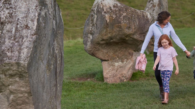 A woman and two children walking among the standing stones at Avebury.